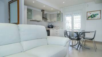 A modern kitchen with white cabinets, a dining table with chairs, and a white sofa in a bright living area.