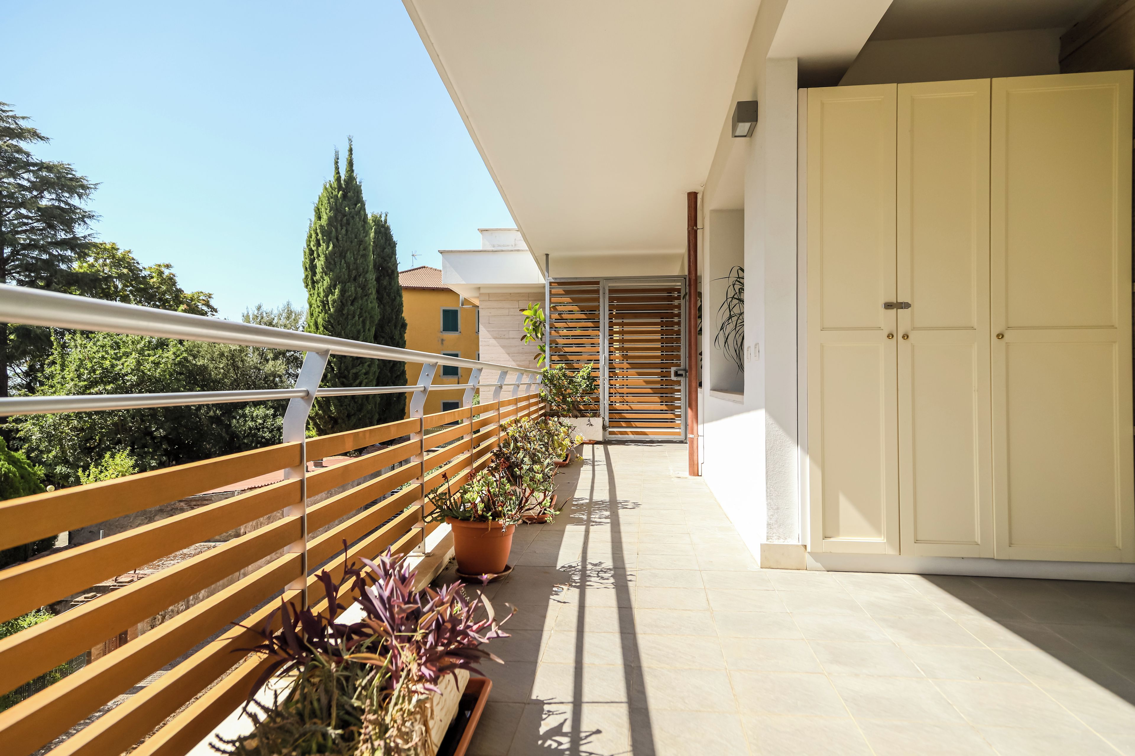 A balcony with a wooden railing, potted plants, and a view of a building in the background.