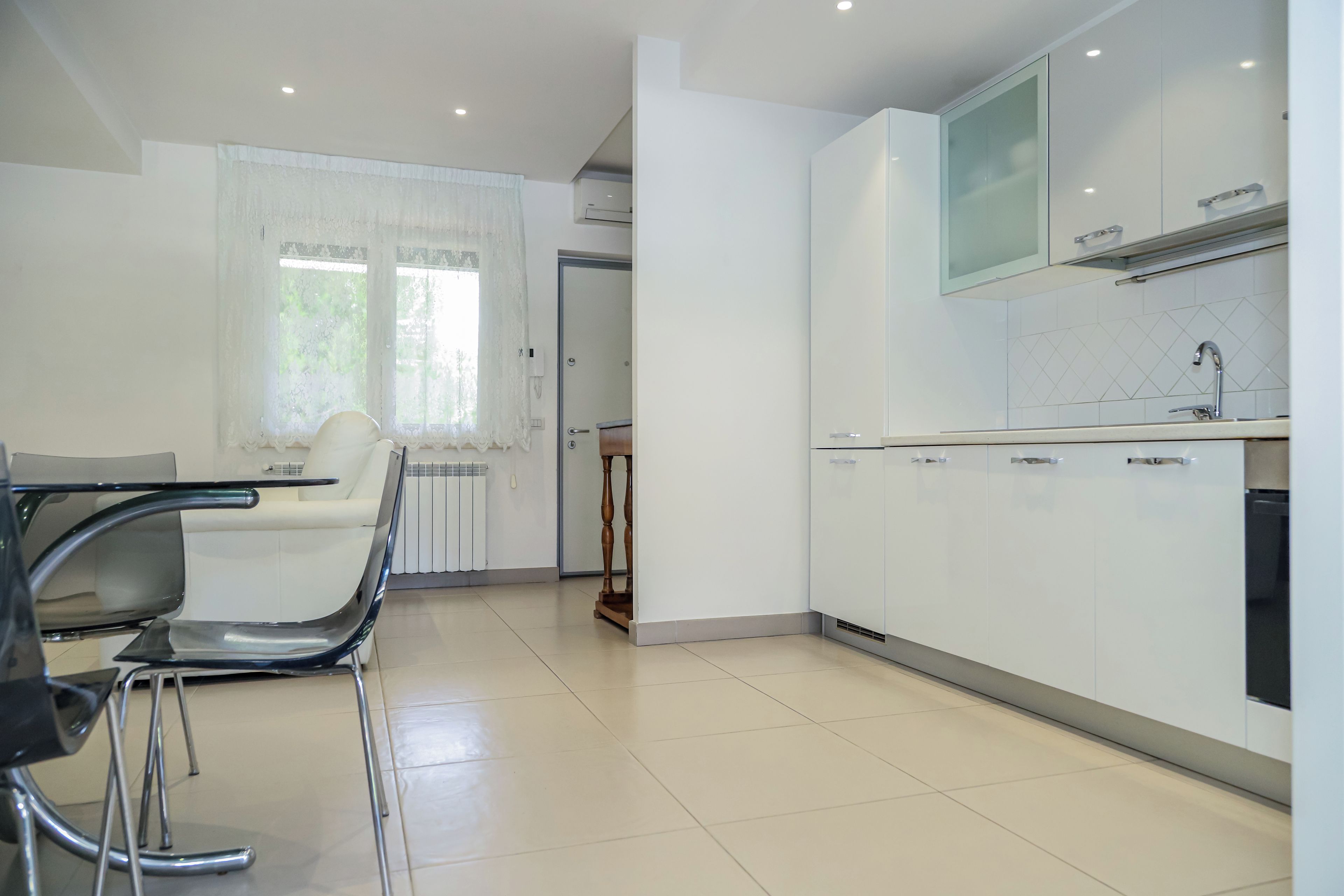 A modern kitchen with white cabinets, a built-in oven, and a window with sheer curtains.