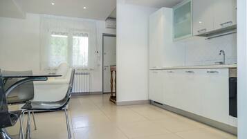 A modern kitchen with white cabinets, a built-in oven, and a window with sheer curtains.