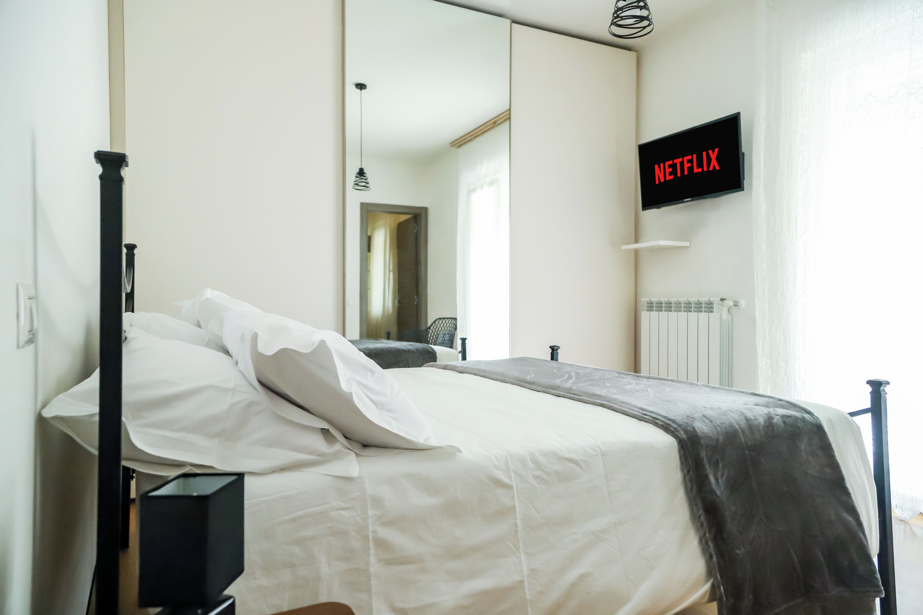 A bedroom with a bed, a television mounted on the wall, and a window.