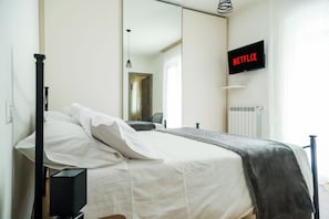 A bedroom with a bed, a television mounted on the wall, and a window.