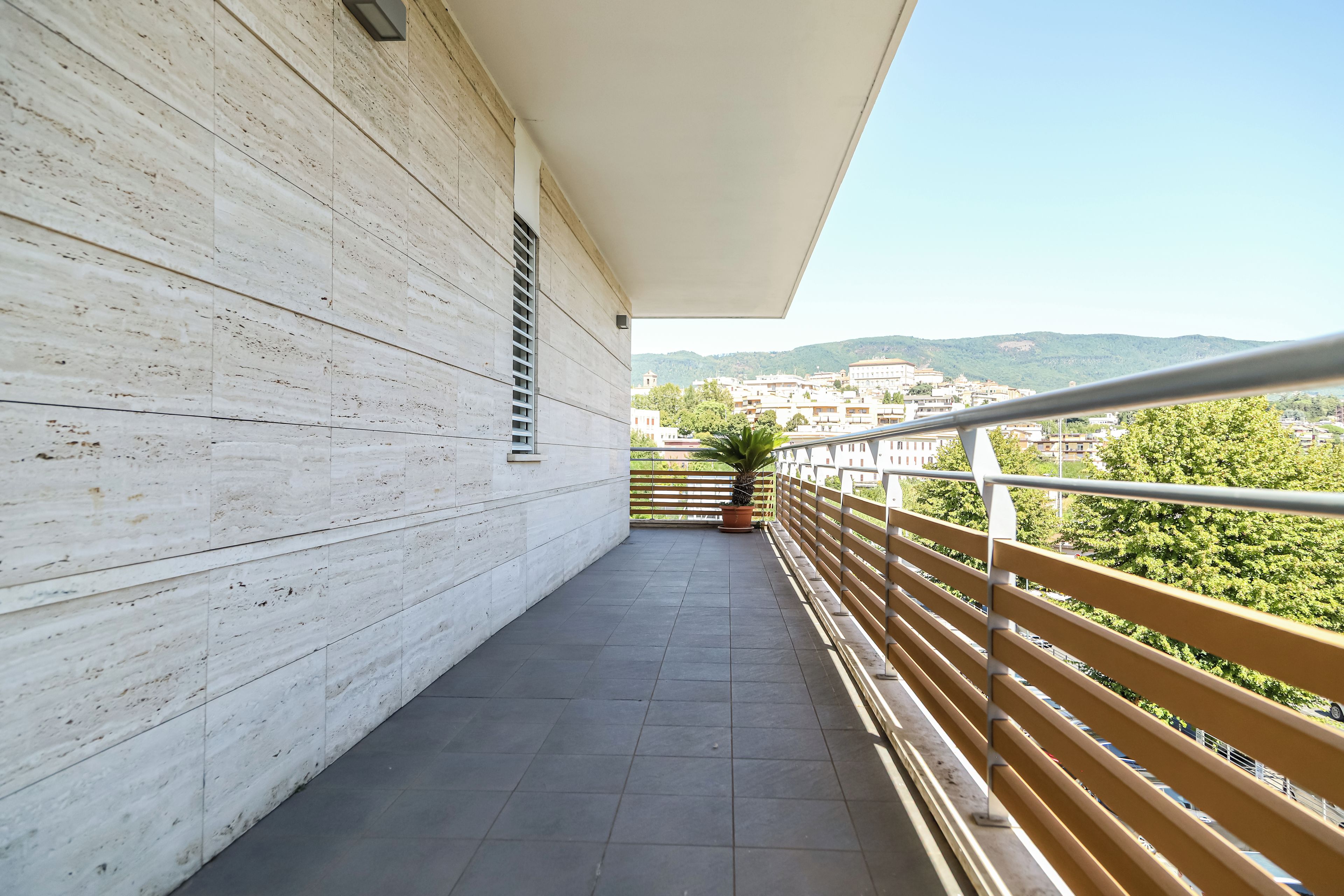 Ein Balkon mit Fliesenboden, Geländer und Blick auf eine Stadt und Hügel in der Ferne.