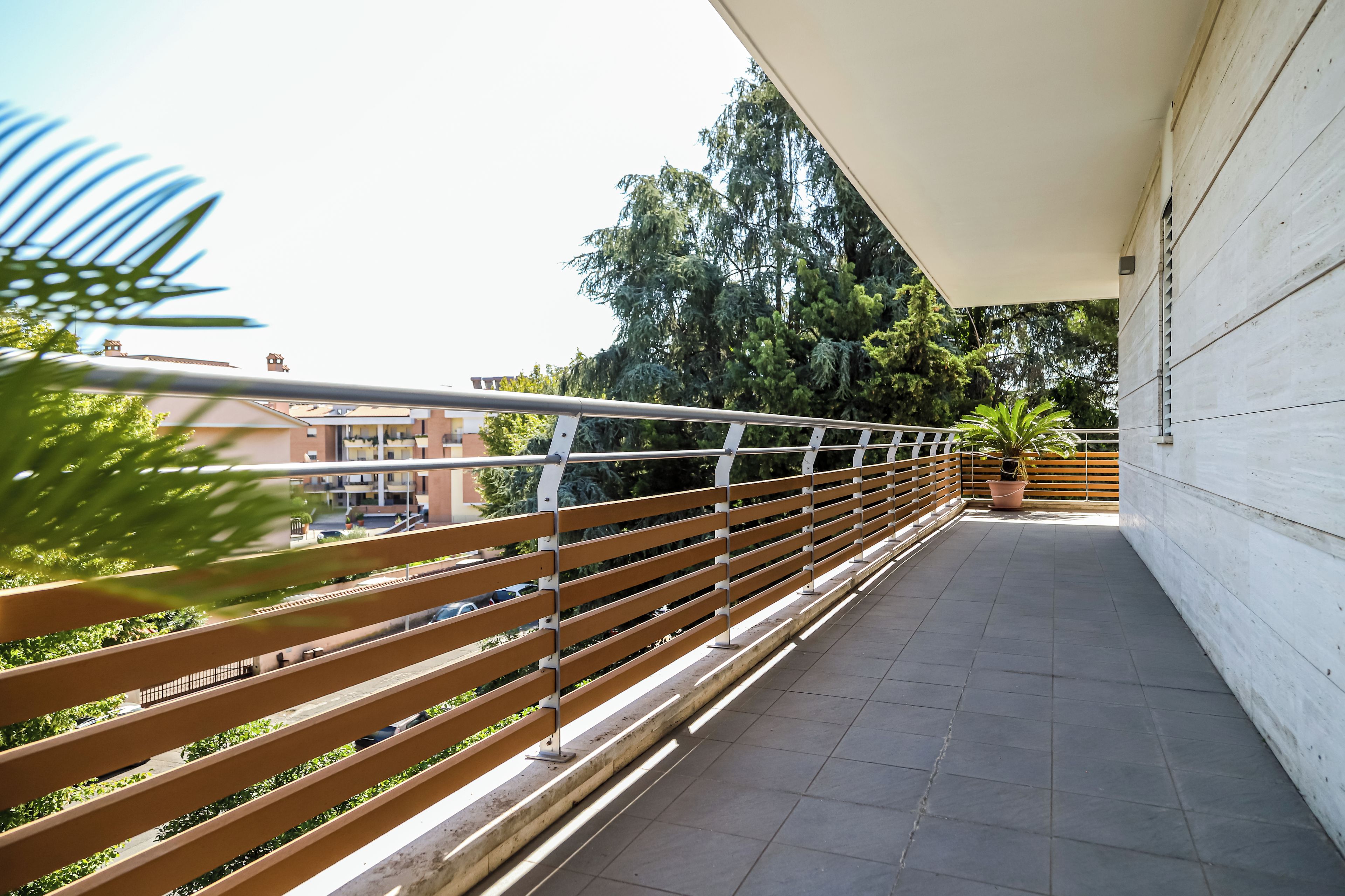A balcony with a metal railing, potted plants, and a view of buildings and trees.