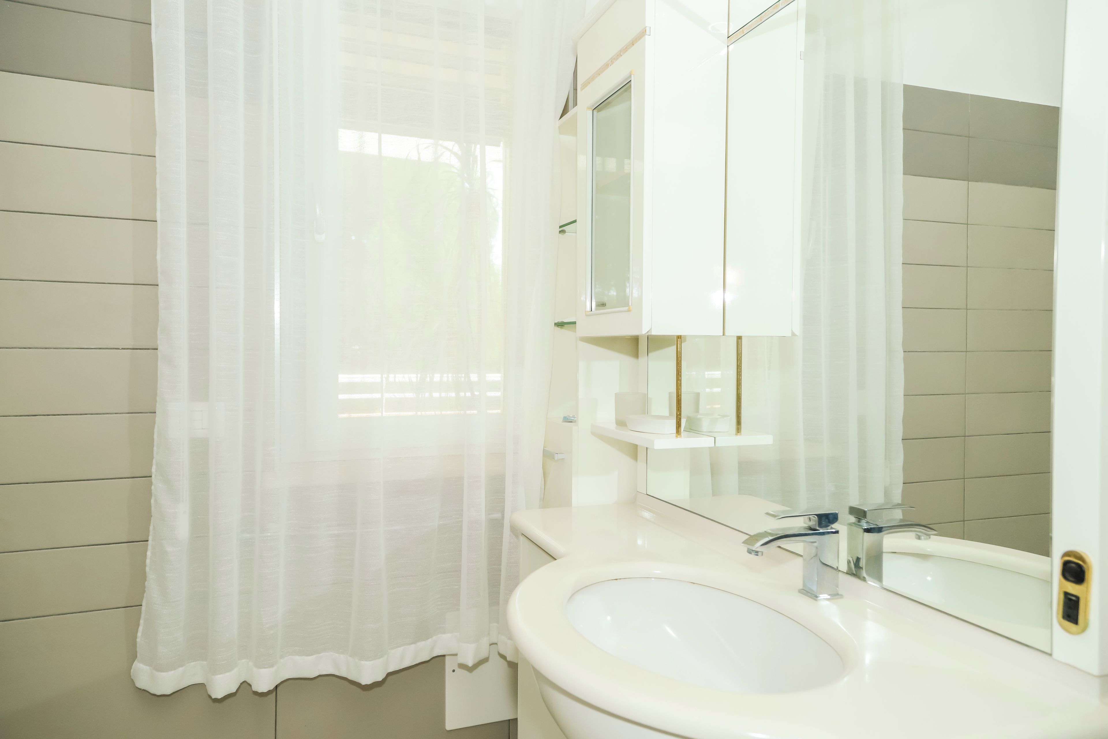 Un baño con un lavamanos blanco, un espejo y una cortina de ducha.