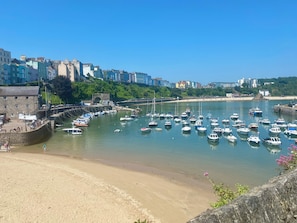 Un pueblo costero con un puerto deportivo lleno de barcos, playa de arena y edificios históricos al fondo.