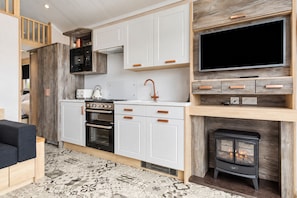A compact kitchen with white cabinets, a stove, and a built-in TV.