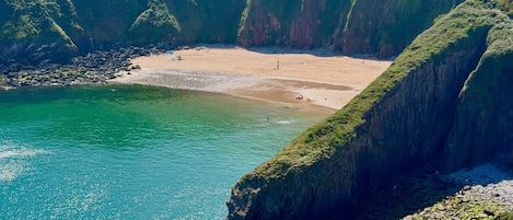 A coastal landscape with cliffs, a beach, and clear turquoise waters.