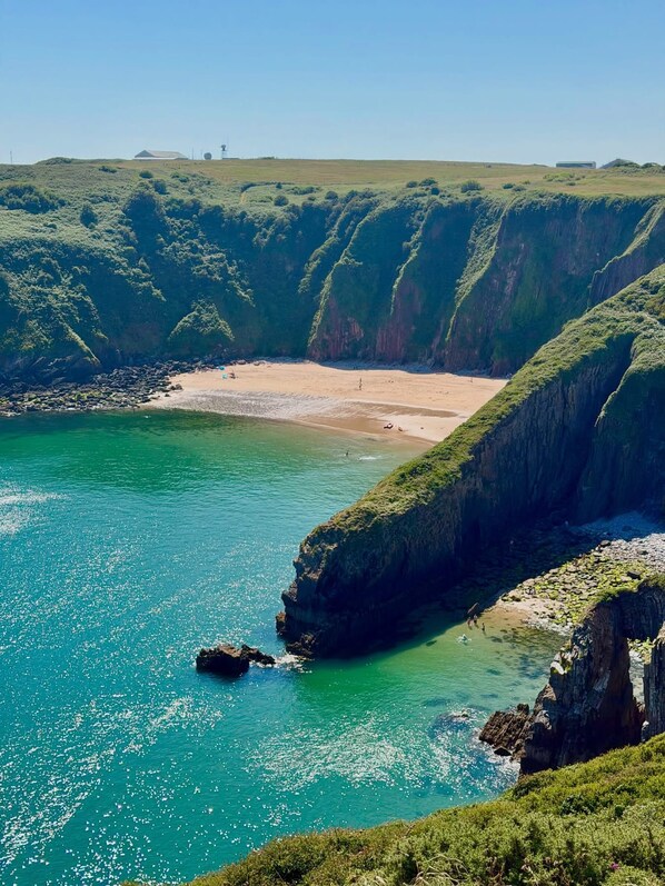 A coastal landscape with cliffs, a beach, and clear turquoise waters.
