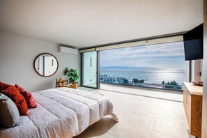 A bedroom with a large bed, a round mirror, a potted plant, and a view of the sea through a sliding glass door. - Aria 3BR Private Jacuzzi & Terrace Nuevo Vallarta (Nuevo Vallarta)