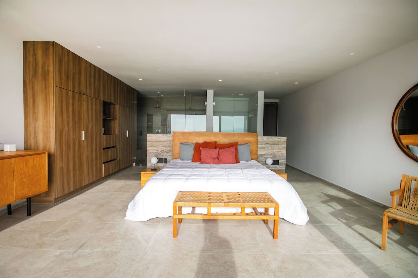 Een moderne slaapkamer met een groot bed, een houten garderobe en een ronde spiegel aan de muur.