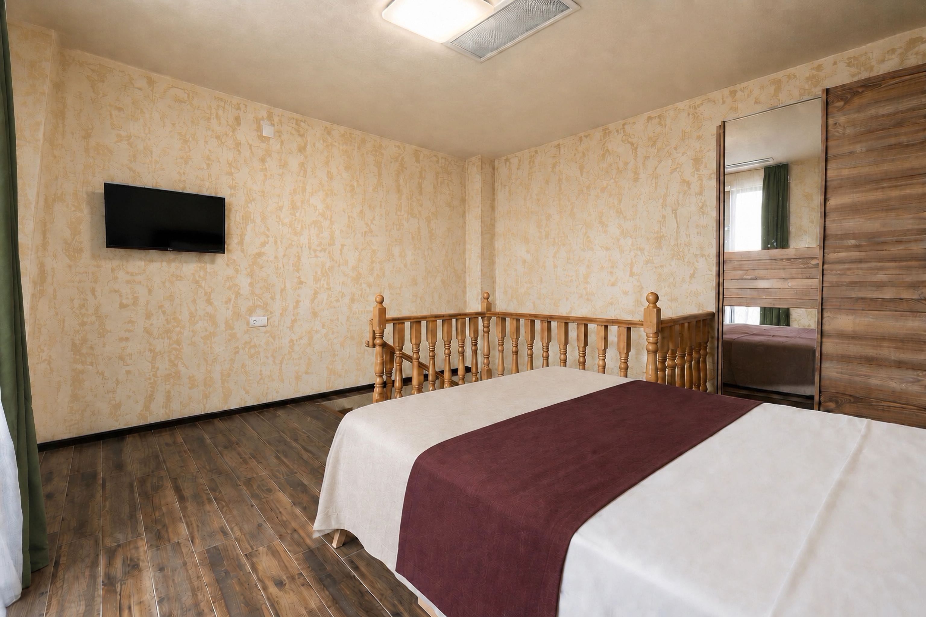 A hotel room with a bed, wooden headboard, a flat-screen TV mounted on the wall, and a mirror on the wall.
