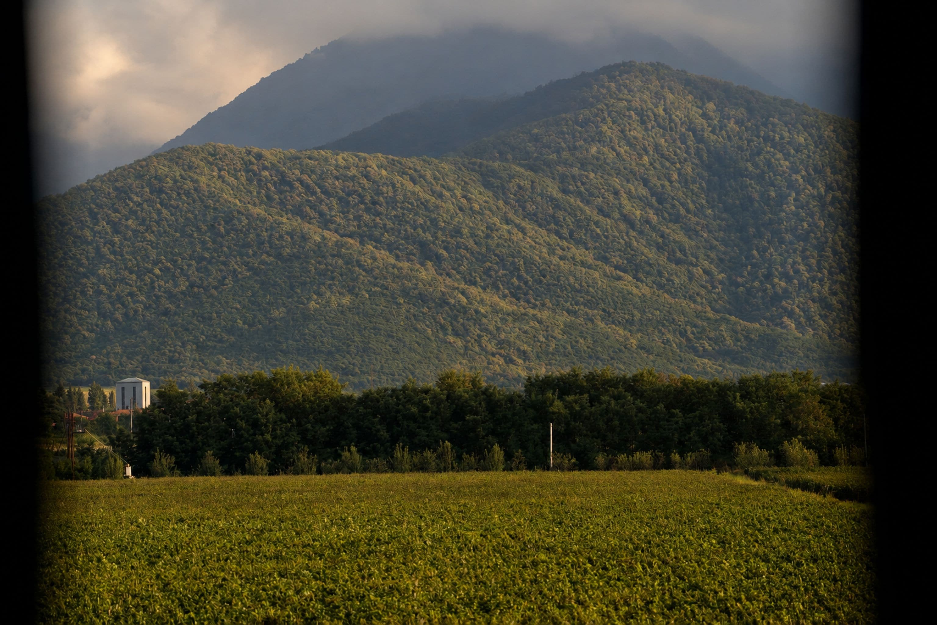 Un paisaje montañoso con un campo en primer plano y un edificio a lo lejos.