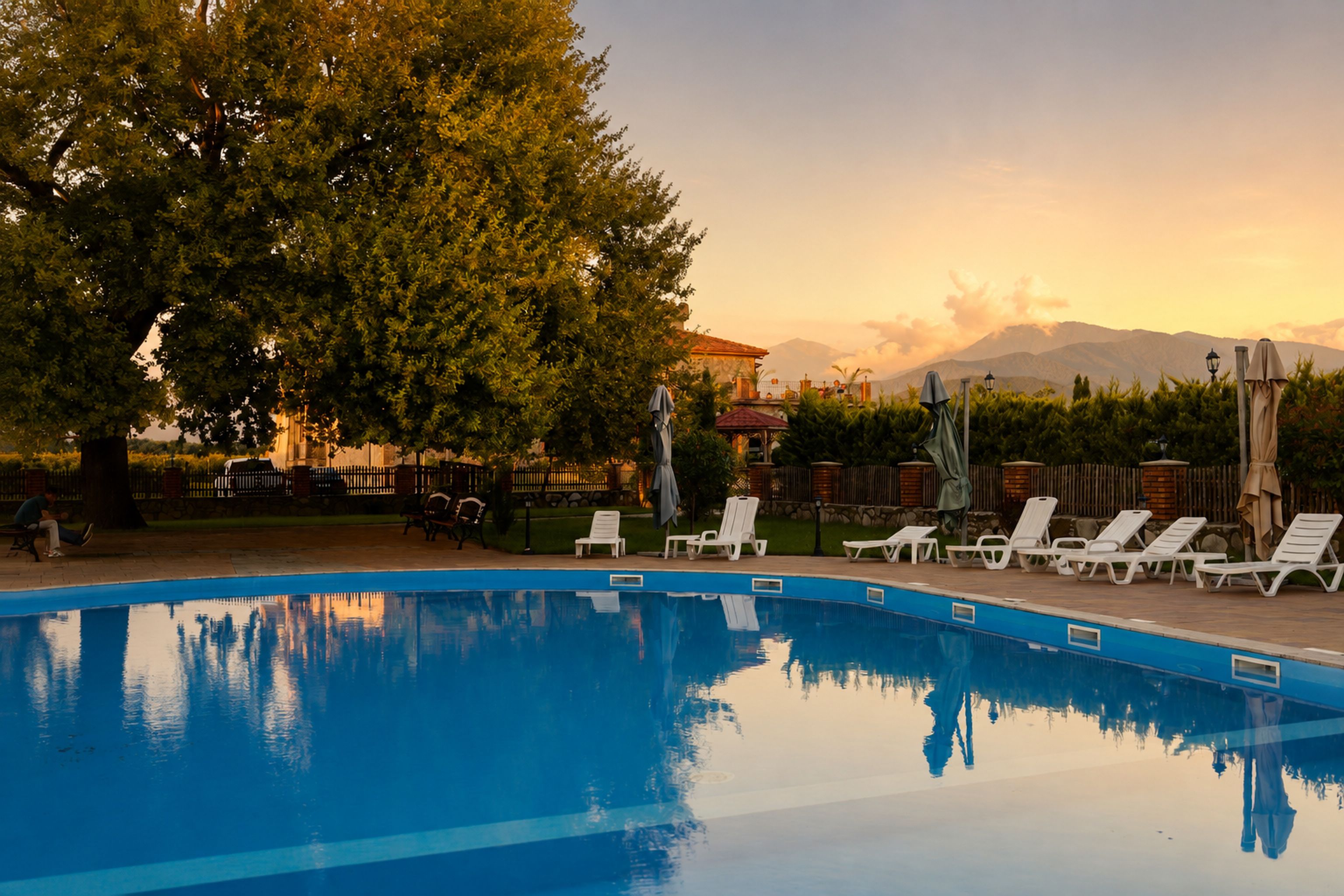 Ein Schwimmbecken mit Liegestühlen und Sonnenschirmen, umgeben von Bäumen und mit Blick auf einen Berg.