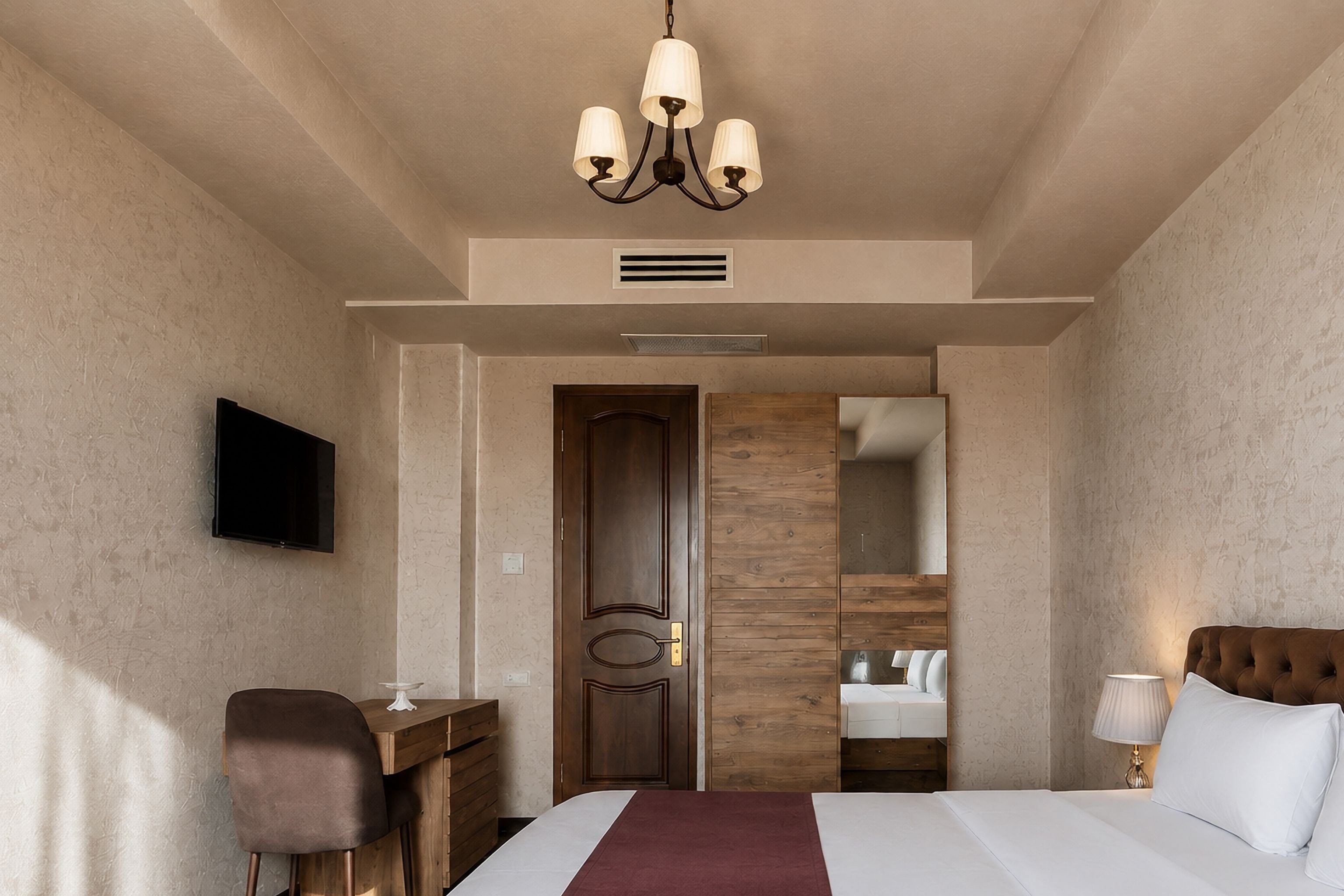Een hotelkamer met een bed, een bureau, een stoel, een televisie, een spiegel en een kroonluchter.