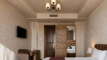 Een hotelkamer met een bed, een bureau, een stoel, een televisie, een spiegel en een kroonluchter.