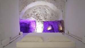 Una cama con vista a un interior que recuerda a una cueva, iluminado con luces moradas.