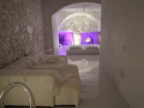 Ein Spa-Raum mit Steinwand, einem Bett mit Kopfteil und Blick auf einen violett beleuchteten Bereich.