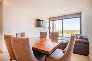 Una sala moderna con una mesa de comedor de madera, cuatro sillas, un sofá y un amplio ventanal con vistas al paisaje.
