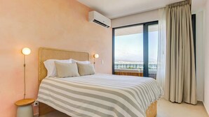 Une chambre d’hôtel équipée d’un lit, d’une lampe de chevet, d’un appareil de climatisation et offrant une vue sur l’extérieur grâce à une grande fenêtre.
