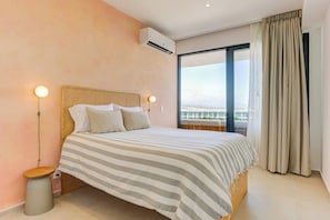 Habitación de hotel con cama, lámpara de noche, aire acondicionado y vistas amplias por una ventana grande.