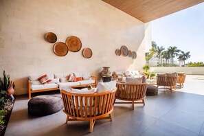 A sunlit outdoor seating area with a sofa and wooden chairs, a wall with circular decorations, and a view of palm trees. - 2 Bedroom with Gorgeous Pool and views at Aria (Nuevo Vallarta)