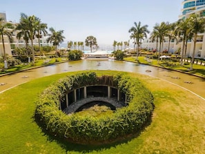 A landscaped pool area with a circular seating area, palm trees, and a view of the ocean. - 2 Bedroom with Gorgeous Pool and views at Aria (Nuevo Vallarta)