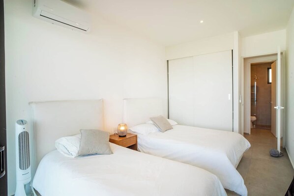 Ein Hotelzimmer mit zwei Betten, einem Nachttisch mit Lampe, einer Klimaanlage und Blick ins Badezimmer.