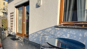 Une terrasse avec une table ronde et une chaise, une porte-fenêtre coulissante et une fenêtre avec des rideaux.