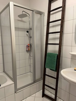 Eine Dusche mit Glastür, eine Holzleiter, ein grünes Handtuch und ein weißes Waschbecken.