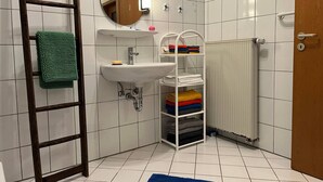 Une salle de bain avec un lavabo blanc, un miroir, un porte-serviettes, un radiateur et un tapis bleu sur le sol.