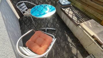 A patio area with a round table and two chairs, a small round table with a cushion, and a wooden bench with a cushion.