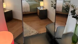 Une chambre à coucher avec un lit, des tables de chevet, un miroir et un vase vert.
