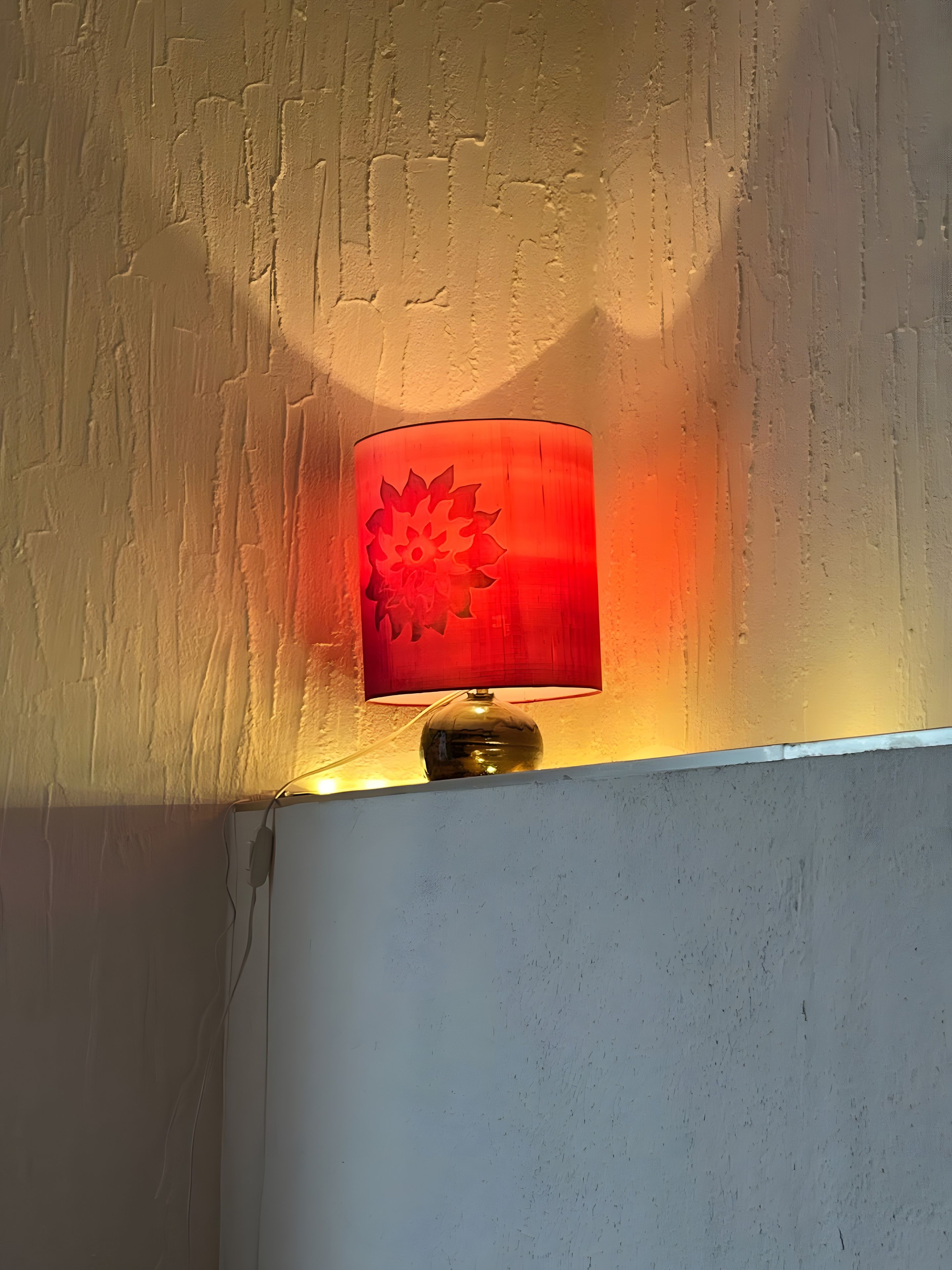 A wall-mounted lamp with a floral design, positioned against a textured wall.