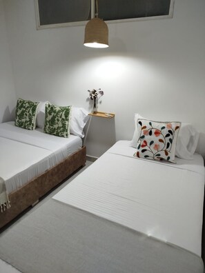 Ein Zimmer mit zwei Betten, einem Nachttisch mit Blumenvase und einer Pendelleuchte.