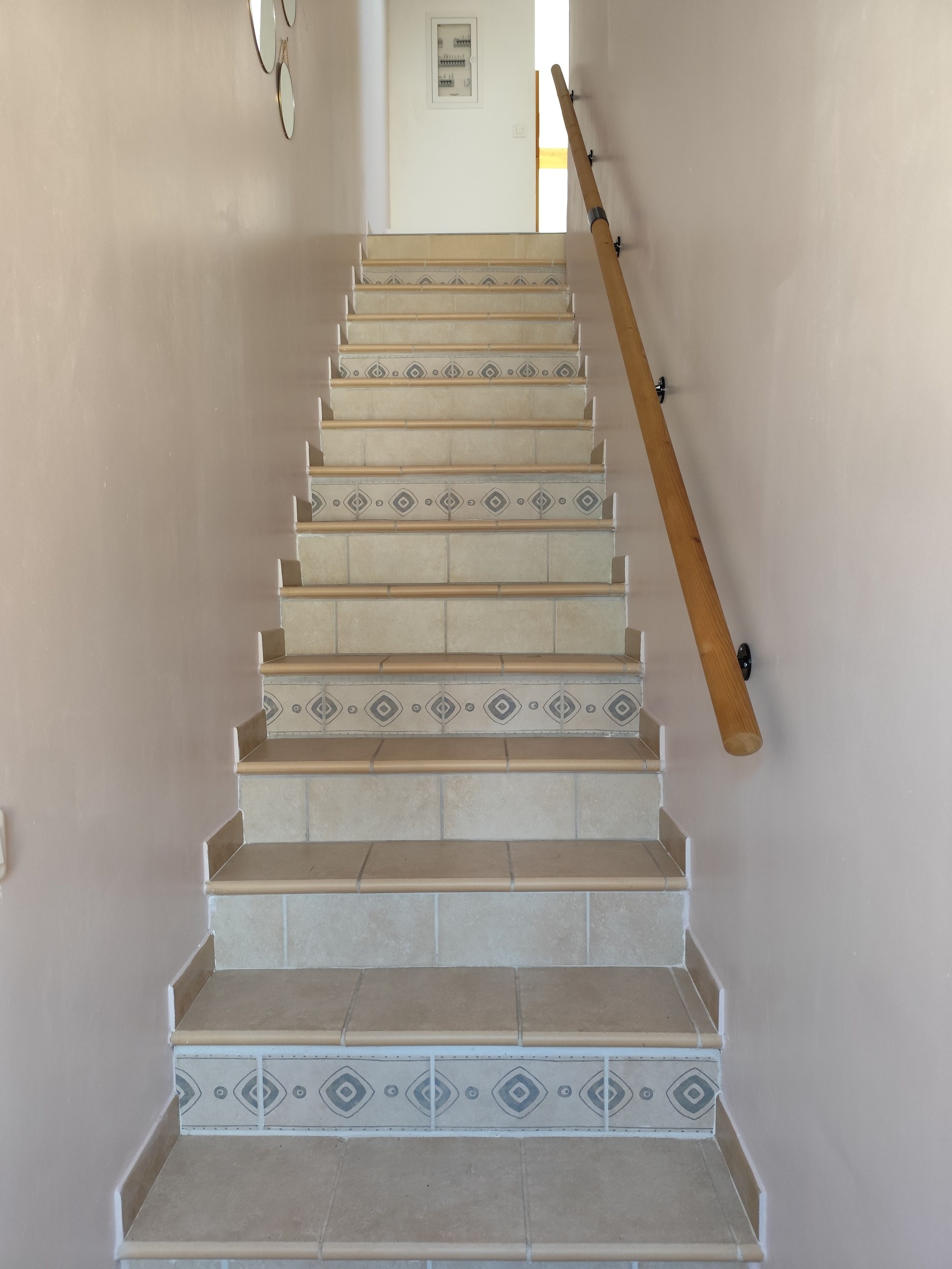 A staircase with patterned tiles and a wooden handrail.