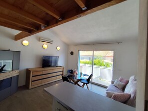 A modern kitchen with a flat-screen TV, wooden cabinets, and a dining area with a table and chairs. - Apartment 'La Salamandre' with Mountain View, Wi-Fi and Air Conditioning (Villelongue-dels-Monts)