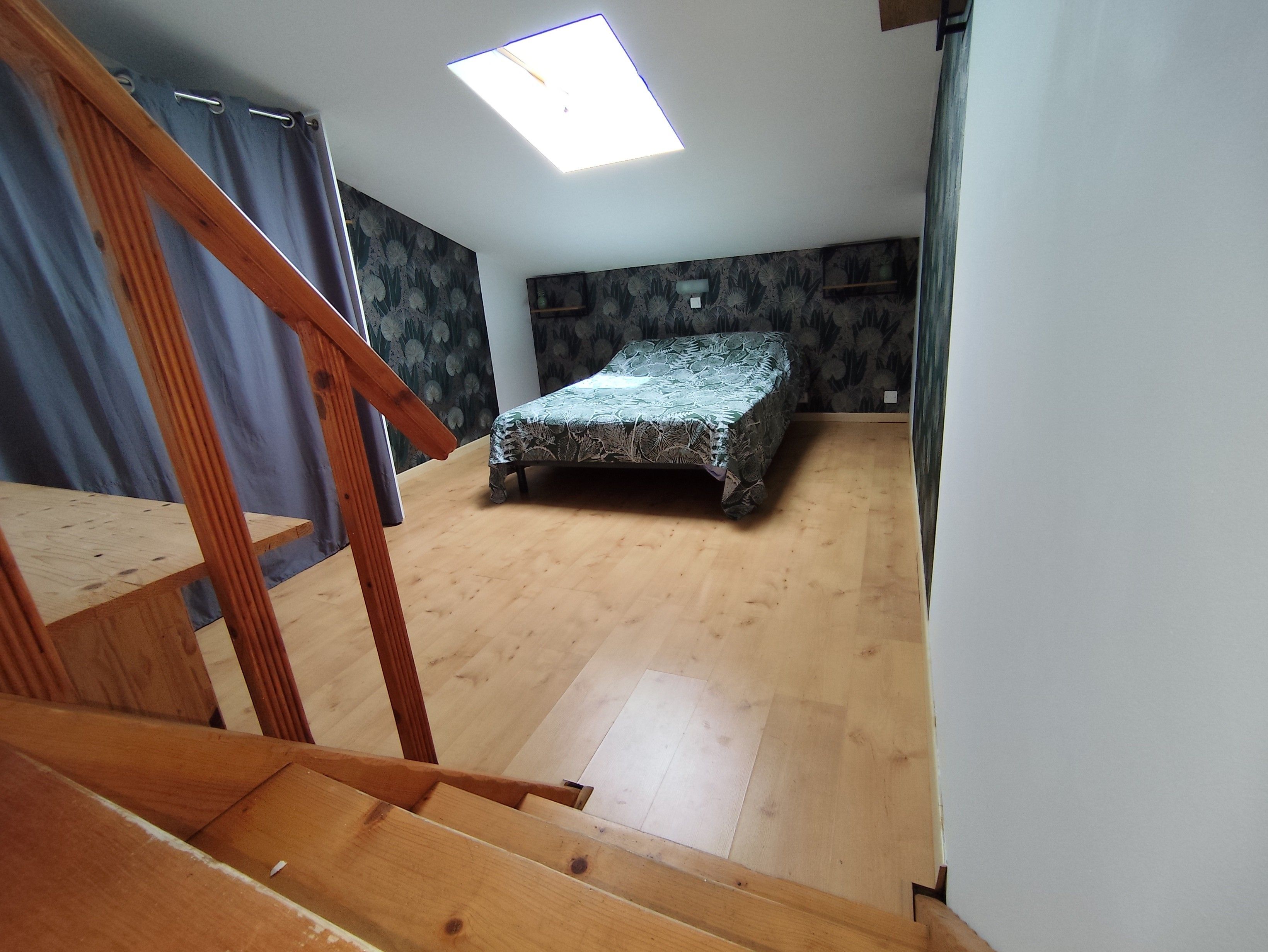 A room with a bed, wooden flooring, a skylight, and a staircase.