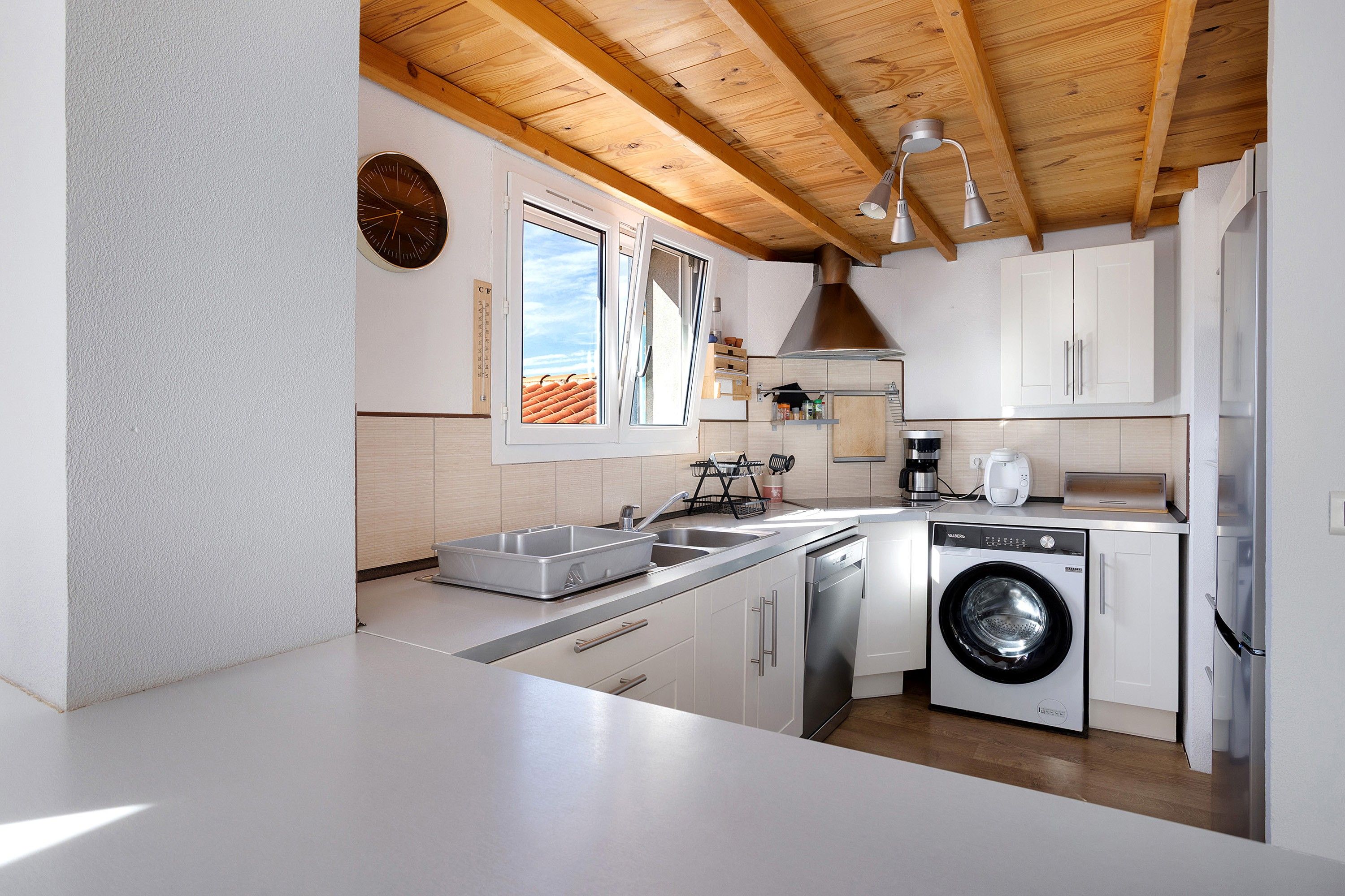 Eine moderne Küche mit Waschmaschine, Spüle und Fenster mit Blick auf das Dach.