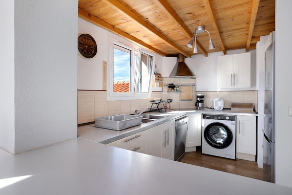 A modern kitchen with a built-in washing machine, a sink, and a window with a view of the roof.