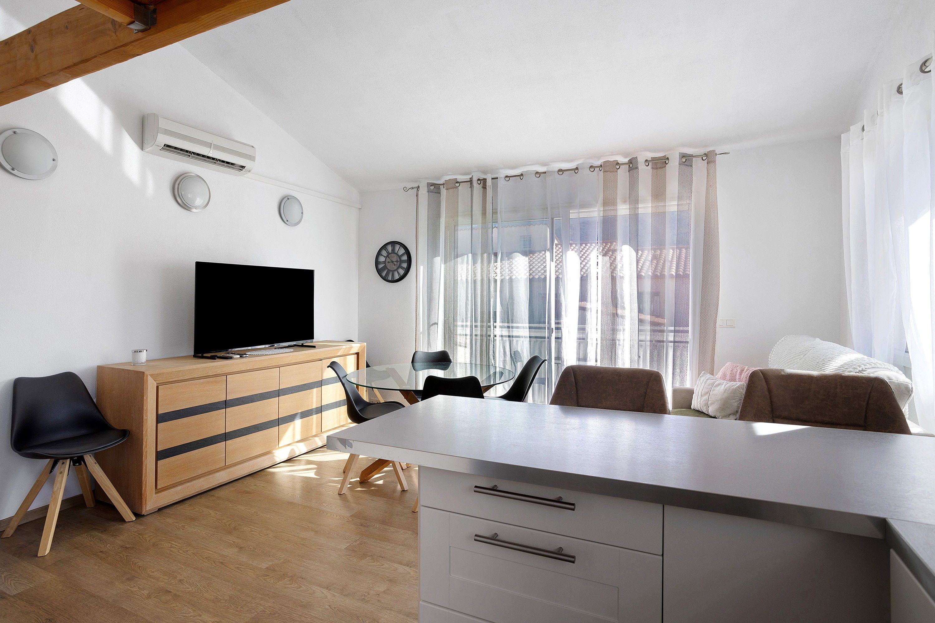 A modern living room with a flat-screen TV, wooden furniture, and a glass dining table.