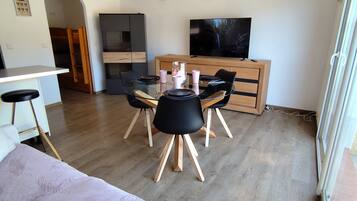 A modern living room with a dining table, chairs, a flat-screen TV, and a wooden ceiling beam.