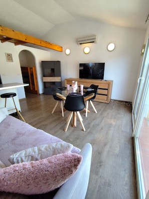 A modern living room with a dining table, chairs, a flat-screen TV, and a wooden ceiling beam. - Apartment 'La Salamandre' with Mountain View, Wi-Fi and Air Conditioning (Villelongue-dels-Monts)