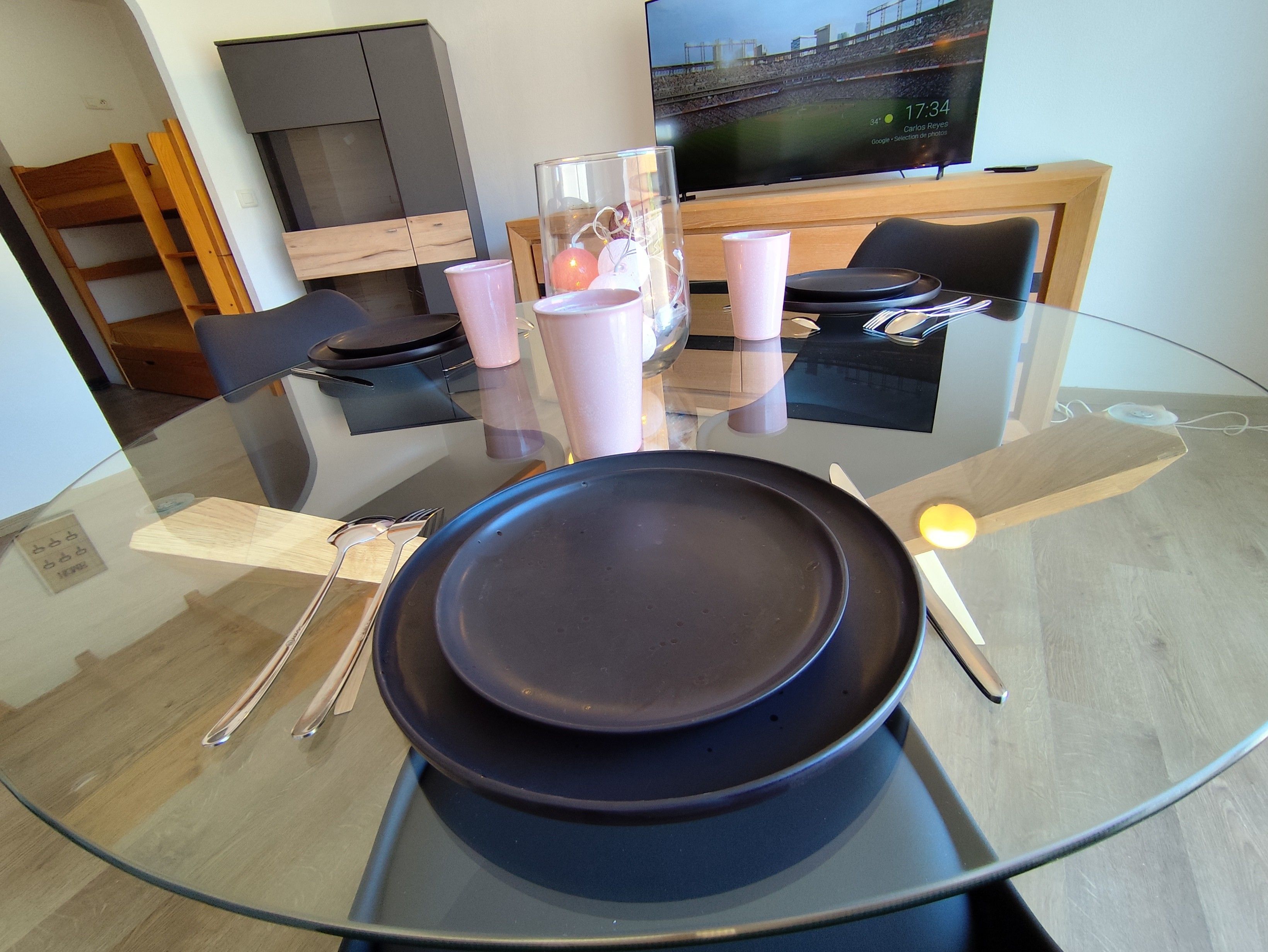 A modern dining area with a glass table, black plates, and pink cups.