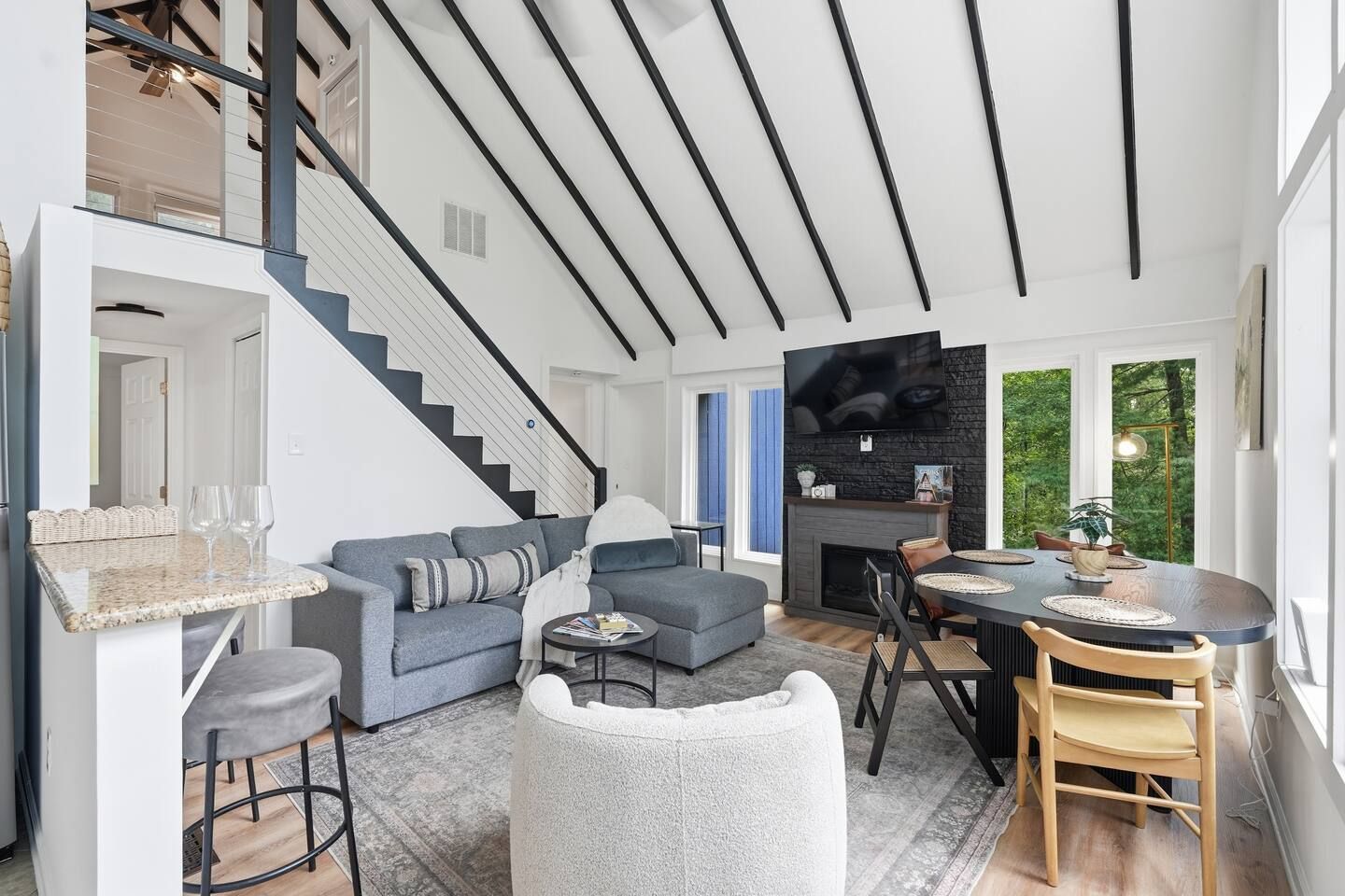 Een modern interieur met een trap, een grijze bank, een eettafel en een open haard.