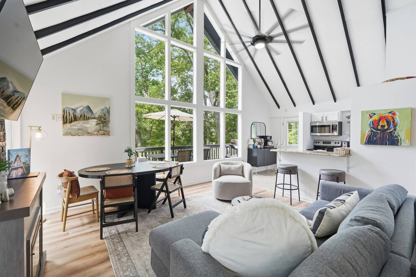 Een moderne woonkamer met een grijze bank, een eethoek met een ronde tafel, en een keuken met een magnetron.