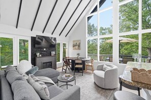 A modern living room with a fireplace, comfortable seating, and large windows offering a view of the outdoors. - A-Frame Soak and Cedar near Skyline Drive and Wineries (Front Royal)