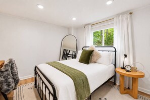 A bedroom with a bed, a bedside table, a mirror, and a window with curtains. - A-Frame Soak and Cedar near Skyline Drive and Wineries (Front Royal)