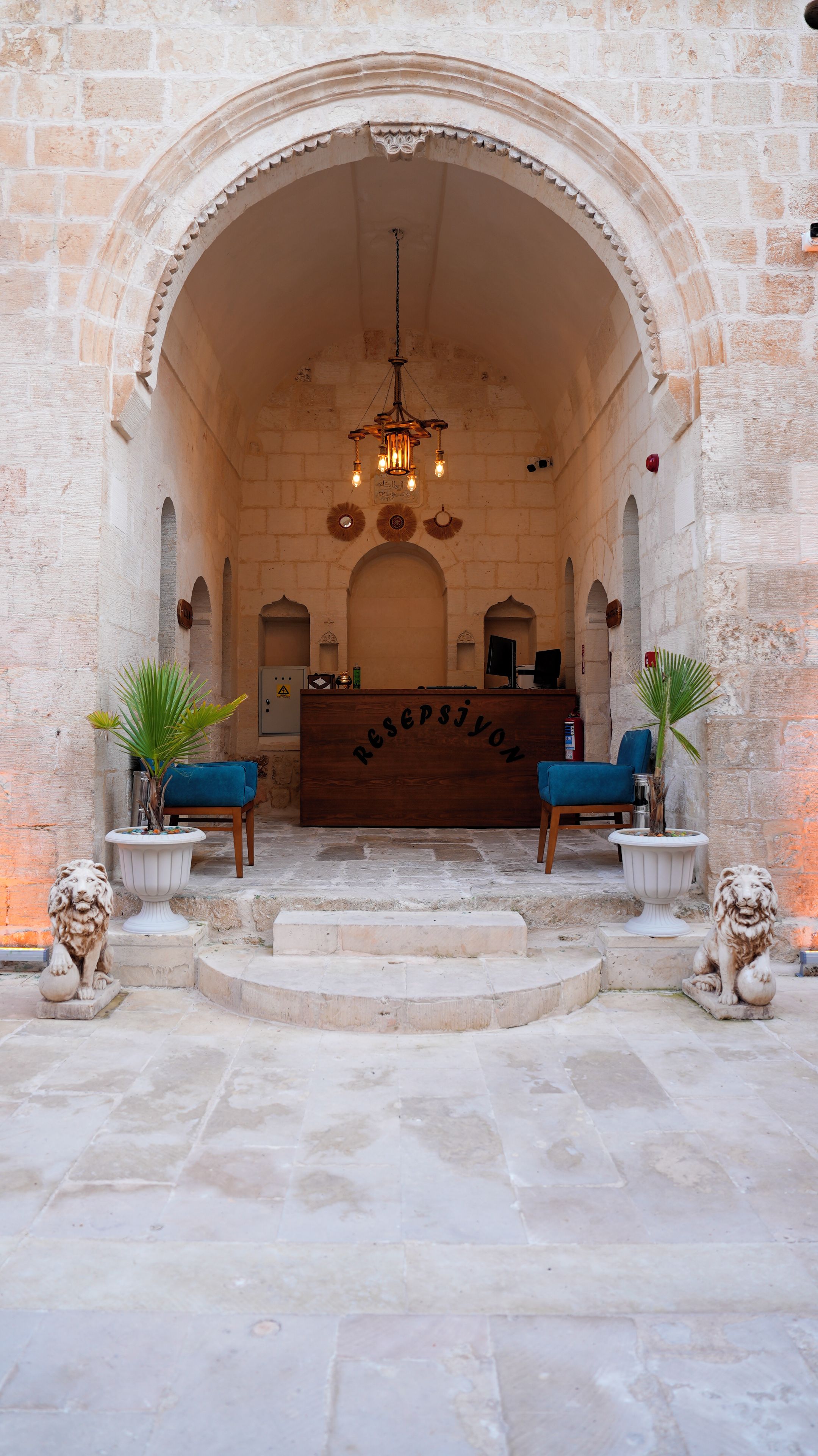 A reception area with a wooden desk, two blue chairs, and a chandelier.