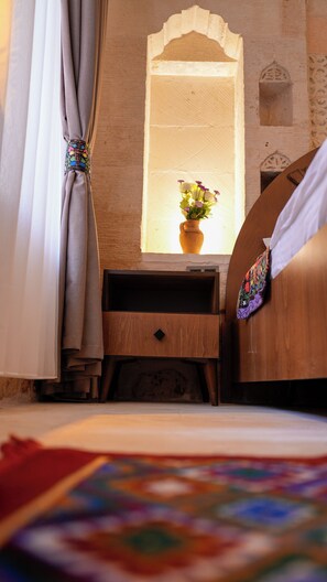A room with a bed, a nightstand with a vase of flowers, and a window with a view of a building. - Sargon Hotel & Cafe (Midyat)